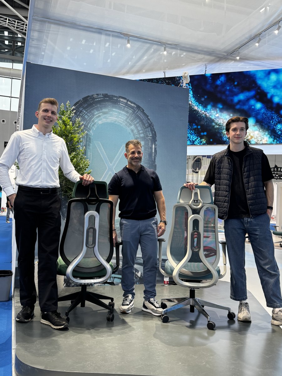 Gustas Šmulkštys ir Lukas Grigalis su ALEGRE Design dizaineriu prie dviejų kėdžių parodos stende