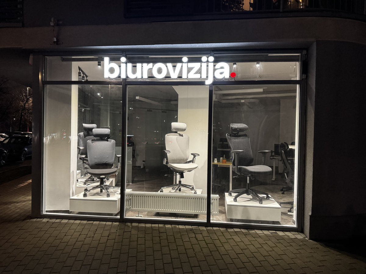 „BiuroVizija“ salonas vakare, biuro kėdės apšviestoje vitrinoje